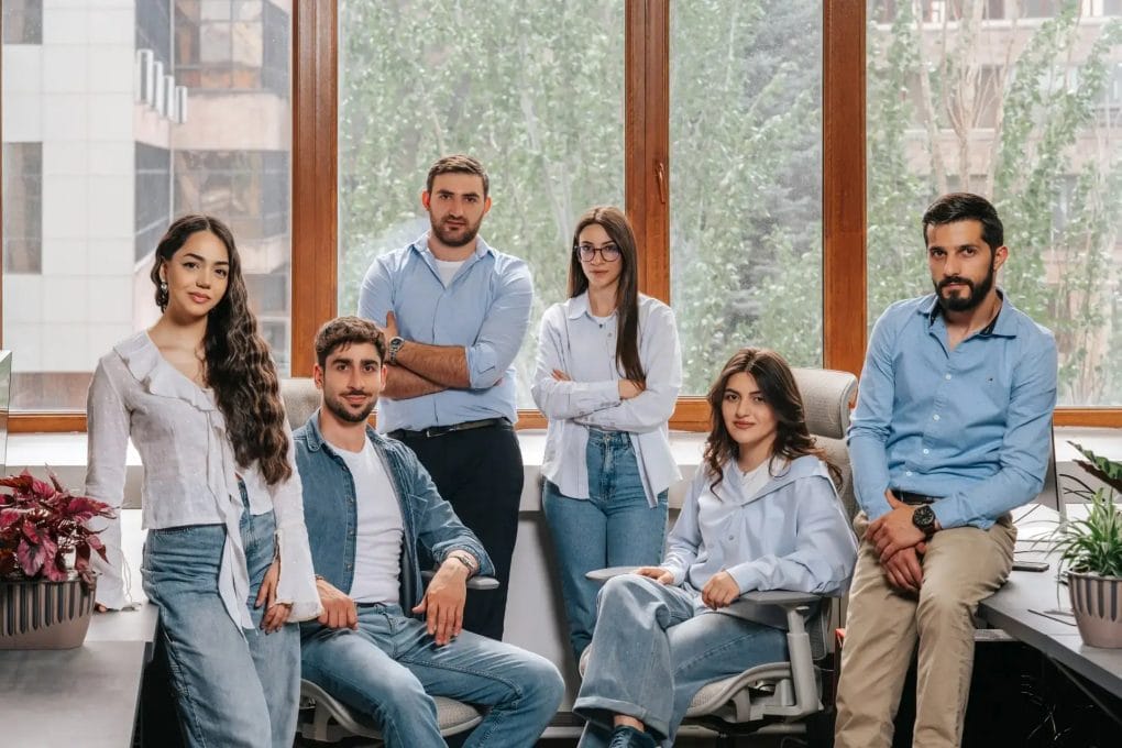 A team of six casually dressed people pose for a professional group photo.